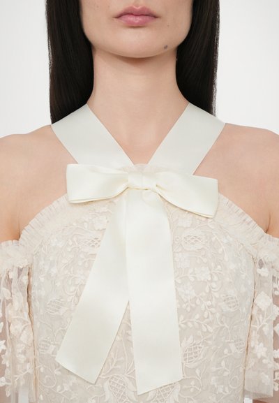 Off-shoulder kant bovenstuk in crème met bloemenpatronen, voorzien van een satijnen strik bij de hals en een gestructureerde, gerimpelde rand.