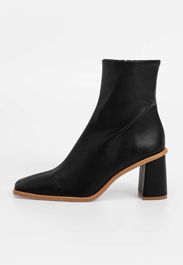 Schwarzer Knöchelstiefel aus glattem Leder, mit eckiger Zehenpartie und einem dicken hohen Absatz mit einer beige Sohle. Einfaches und modernes Design.