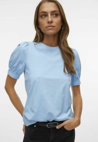 T-shirt de algodão azul claro com mangas curtas em balão, decote redondo e um corte descontraído. Combinado com jeans pretos e um cinto preto.