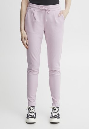 Jogger rosa chiaro con vita regolabile, tasche laterali e taglio affusolato, realizzati in tessuto morbido. Indossati con sneakers alte nere.