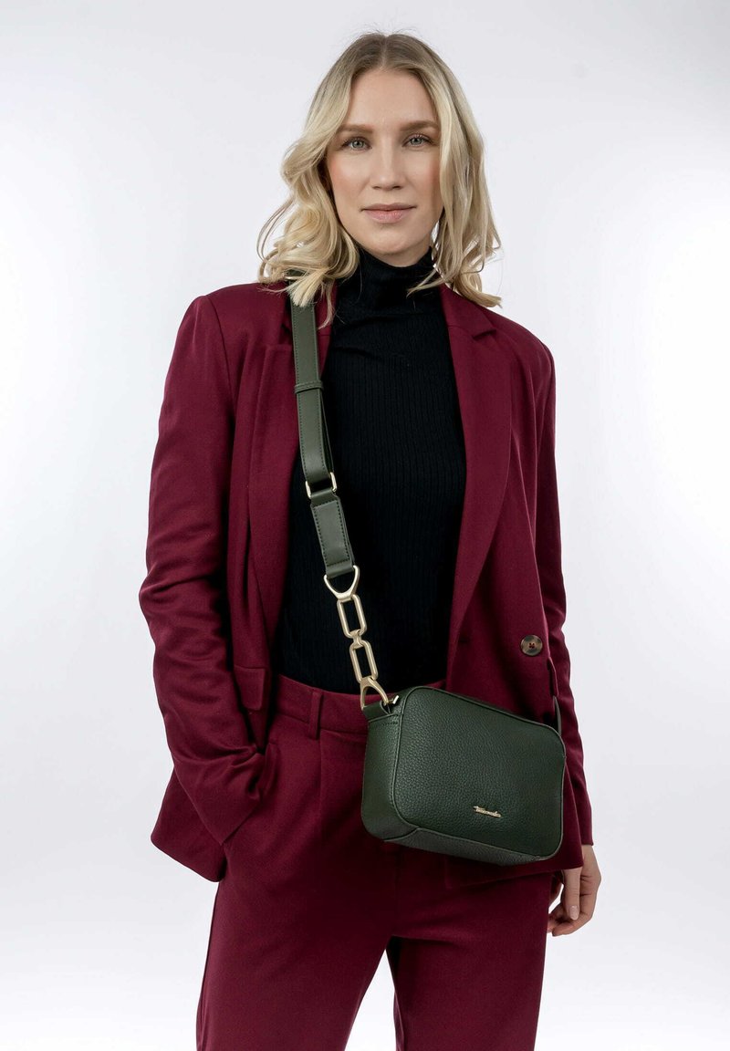 Borsa a tracolla verde in pelle con finitura testurizzata, hardware dorato e tracolla regolabile. Indossata da una persona con un completo bordeaux.