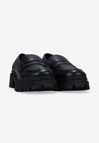 Zapatos de cuero negro con punta redondeada, suela de goma gruesa y diseño de tiras en capas en la parte frontal. Detalles acentuados con surcos en la suela.