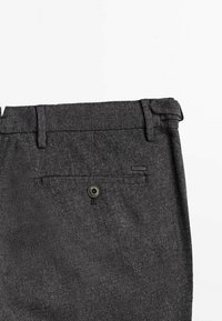 Mörkgrå, texturerad tyg av skräddarsydda byxor, med en bakficka med knapp och en liten märkesetikett sydd ovanför fickan.