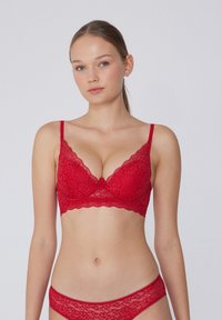 Sujetador de encaje rojo con bordes festoneados, varilla y tirantes ajustables. Presenta un patrón floral y un tanga de encaje a juego.
