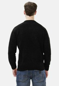 Maglione nero con texture a maglia spessa, polsini e orlo a coste, e un classico collo a giro, indossato con jeans blu.