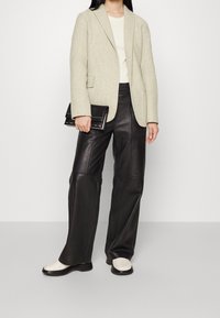 Světle šedý texturovaný blazer, krémový top, černé kožené kalhoty širokého střihu a krémové slip-on boty s černou podrážkou a černou kabelkou.