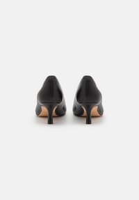 Chaussures à talons hauts en cuir noir avec un bout pointu, un talon stiletto slim et une texture lisse, vues de l'arrière.