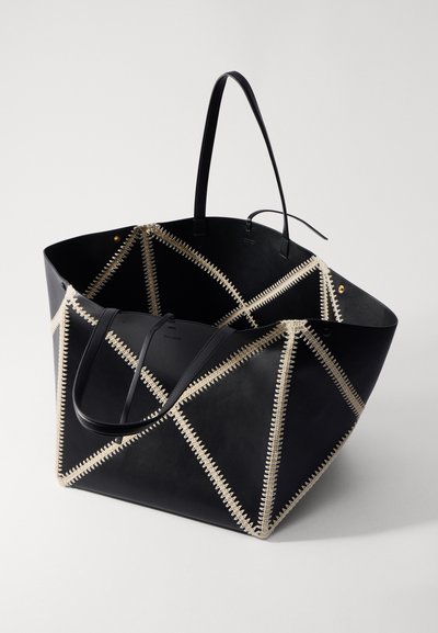 Black leather tote bag with diagonal cream stitching, featuring two handles and an open top. Shaped as a wide triangle.
