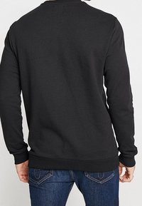 Schwarzer Pullover mit langen Ärmeln, geripptem Rundhalsausschnitt sowie dehnbarem Saum und Bündchen; gefertigt aus weichem, strukturiertem Stoff.