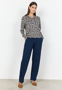 Blusa a maniche lunghe con motivo in crema, blu navy e ruggine, abbinata a pantaloni palazzo blu navy. Scarpe con tacco alto in suede marrone completano l'outfit.