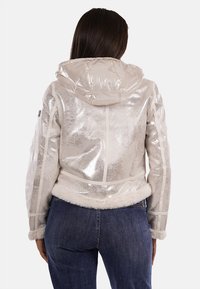 Giacca puffer metallica argento con cappuccio, bordo in pelliccia sintetica all'orlo e dettagli sulle cuciture. Tessuto morbido con finitura lucida.