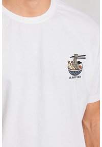 Biała bawełniana koszulka z grafiką miski z makaronem, krewetkami i jajkiem, pałeczkami oraz napisem "KAOTIKO" poniżej wzoru.