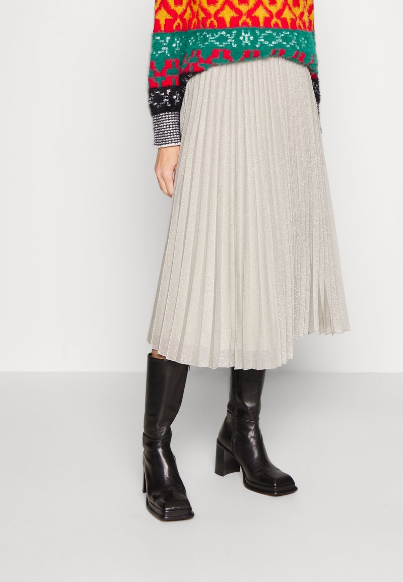 Falda midi plisada en gris claro con un suave brillo, combinada con botas de tacón de cuero negro hasta la rodilla.