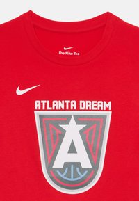 Raudona medvilninė marškinė su „ATLANTA DREAM“ tekstu ir logotipu pilkos, baltos ir mėlynos spalvų. Prekės ženklas yra kairiajame viršutiniame kampe.