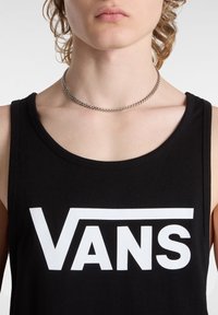 Mustat puuvillapaitatoppit, jossa on suuri valkoinen "VANS"-logo. Ominaisuudet pyöreä kaula-aukko ja hihaton muotoilu. Hopeinen ketjun kaulaketju on näkyvissä.