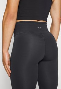 Black leggings with a high waistband feature a smooth, stretchy fabric. The brand "casall" is displayed on the waistband.