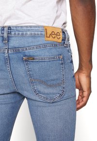 Blå denimjeans med en läderetikett "Lee" vid midjan, med bakfickor med krökt sömnad och en slim fit-design.