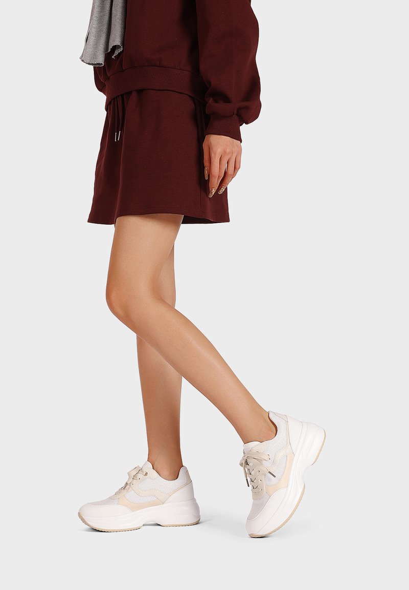 Sneaker bianchi e beige con materiali in rete e sintetici, forma arrotondata, cuciture intricate e suole testurizzate.