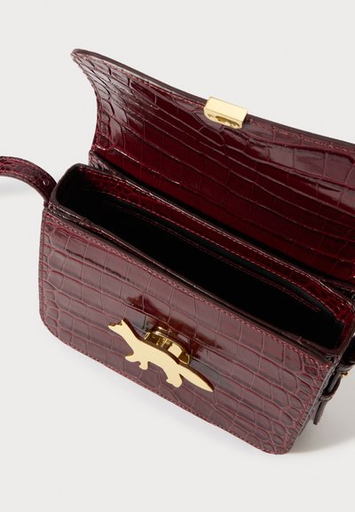 Σκούρο κόκκινο δερμάτινο τσάντα με υφή κροκοδείλου, με ανοιχτό καπάκι και χρυσό κούμπωμα σε σχήμα αλιγάτορα, που αποκαλύπτει κενές εσωτερικές θήκες.