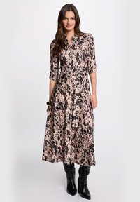 Abito midi in una stampa astratta rosa e nera, caratterizzato da un colletto, una chiusura a bottoni e una cintura in vita. Abbinato a stivali neri al ginocchio.
