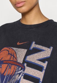 Hanorac din bumbac negru, cu un grafic mare de baschet colorat mult și literele "NIKE" în tonuri contrastante de albastru și piersică.