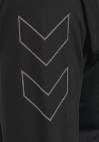 Svart atletisk tröja med tre nedåtriktade chevron-mönster i grått på vänster ärm. Tillverkad av ett slätt, stretchigt tyg.