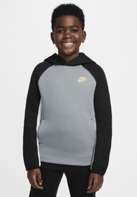 Sudadera Nike con un frente gris, mangas raglán negras y un logo amarillo en el pecho. Tela suave con un ajuste casual y capucha con cordón.