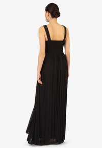 Zwarte maxi-jurk met een smock-bustier, brede schouderbanden en een vloeiende geplooide rok. Gemaakt van lichte stof voor een soepele textuur.