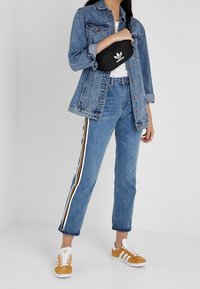 Blue denim jacket, white t-shirt, blue jeans with yellow and black stripes, and brown and white sneakers. Black Adidas belt bag is worn.