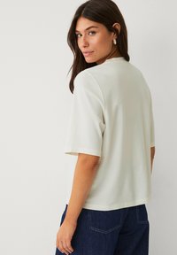Haut beige clair à manches courtes en tissu doux, avec un col rond et une coupe décontractée, associé à un bas en denim bleu foncé.