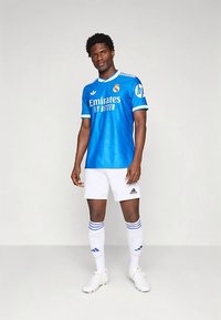 Niebieska koszulka piłkarska z białymi akcentami, z logo i napisem „Emirates Fly Better”, w połączeniu z białymi spodenek i skarpetkami z niebieskimi paskami.