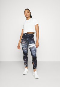 Sort og blå mønstrede leggings med orange accenter og en sort talje, parret med en hvid cropped t-shirt og hvide sneakers.