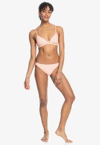 Bikini set s tenkými ramienkami v svetlej broskyňovej farbe s bielymi vertikálnymi pruhmi; obsahuje trojuholníkový vrch a nízko nasadené spodky, hladká textúra.