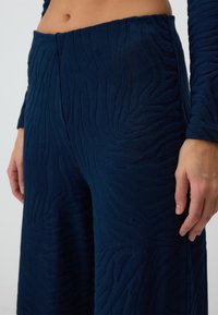 Donkerblauwe wijde broek gemaakt van textiel met een verhoogd golfpatroon. Heeft een hoge taille en een relaxte pasvorm met zijzakken.