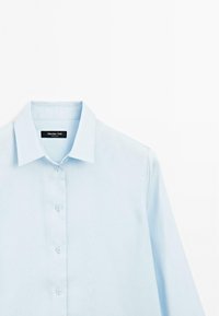 Camicia azzurro chiaro con colletto a punta, caratterizzata da una texture liscia e un piccolo etichetta logo all'interno del colletto.
