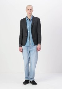 Črn blazer preko svetlo modre denim srajce, v kombinaciji s svetlo modrimi kavbojkami in črnimi supergami. Enostaven dizajn, strukturiran kroj in mehki materiali.