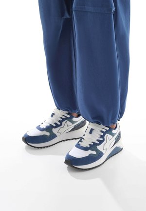 Scarpe da ginnastica blu e bianche realizzate in suede e materiali a rete. Presentano un logo bianco distintivo e una suola nera texturizzata.