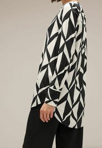 Camicia a maniche lunghe bianca e nera con motivo geometrico, dotata di orlo curvo e polsini con bottoni, realizzata in un tessuto liscio.