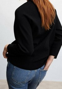 Černý pletený svetr s kulatým výstřihem, tříčtvrtečními rukávy a přiléhajícím lemem, nošený přes modré džíny s klasickými kapsami.