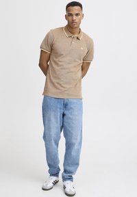 Brown polo shirt with contrast collar, paired with light blue baggy jeans. Model wears white sneakers with black accents.