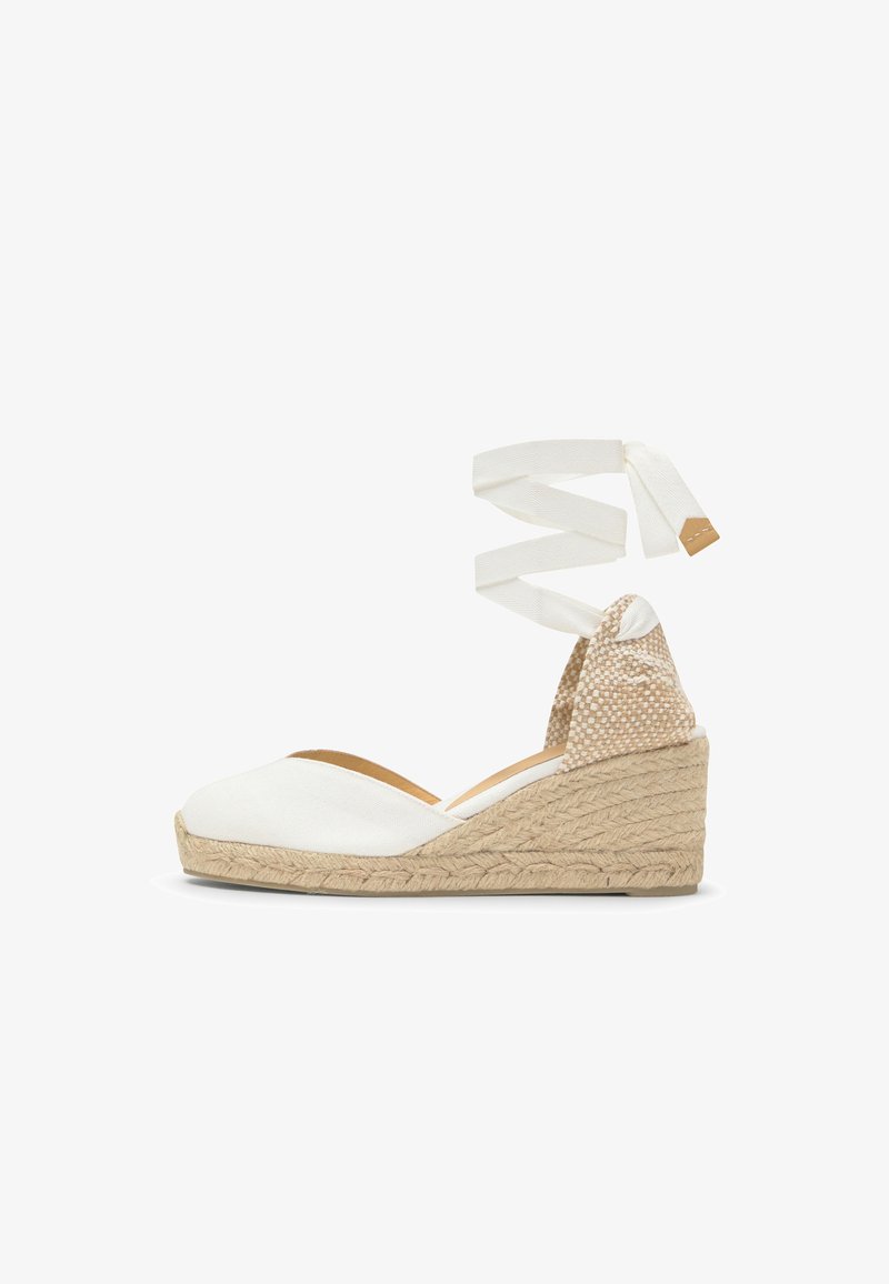 Espadrille compensée avec talon tressé beige, bout fermé blanc, et longues lanières blanches à nouer autour de la cheville sur fond blanc.