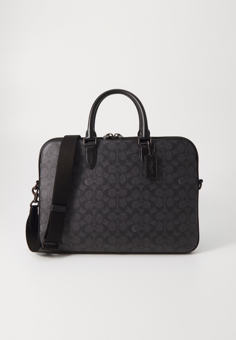 Black leather bag with a subtle patterned design, dual top handles, removable shoulder strap, and zip closure. Features a tag with branding.