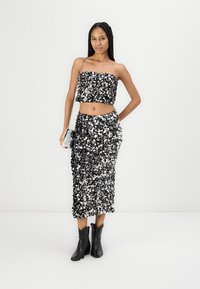 Conjunto de dos piezas en negro y plateado con lentejuelas, que incluye un top corto y una falda ajustada. Combinado con botas negras de tobillo y un pequeño bolso plateado.