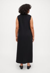 Black sleeveless maxi dress with a smooth texture, featuring a straight cut and a back seam. Paired with black mesh-detail shoes.