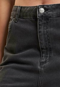 Black denim jeans featuring a high waist, front fly closure with a silver button, and detailed stitching along the seams.