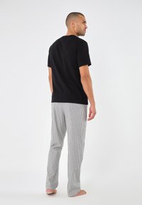 Sort kortærmet t-shirt parret med grå og hvide stribede bukser. Bukserne har en løs pasform og lige ben-design.