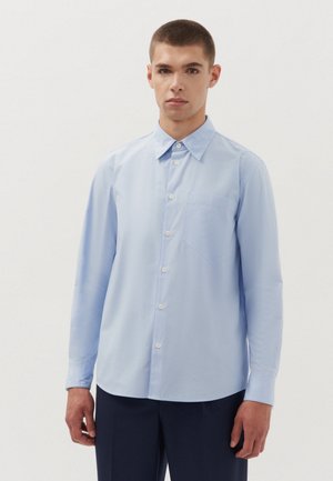 Chemise à manches longues bleu clair en tissu lisse, dotée d'un col boutonné, d'une poche avant et d'une base droite.
