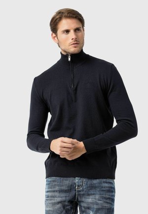 Dunkelblaue Halb-Zip-Strickjacke aus gestricktem Stoff. Sie verfügt über einen gerippten Kragen und Bündchen sowie über eine dezente Markenkennzeichnung auf der Brust.