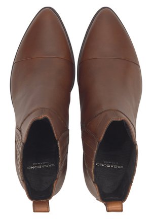 Braune Leder-Stiefeletten mit spitzer Kappe, seitlichen elastischen Einsätzen und einem dezenten Absatz. Glatte Textur und minimale Nähte.