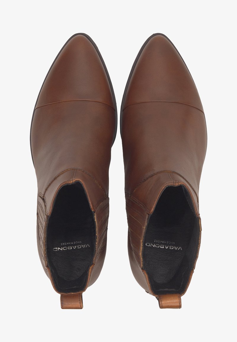 Bottines en cuir marron avec un bout pointu, dotées de panneaux élastiques sur les côtés et d'un petit talon. Texture lisse et détails de couture minimaux.